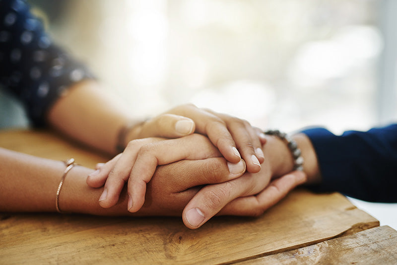 Two pairs of hands clasped together on a wooden surface with a blurred background